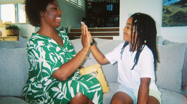 A POC mother and child high fiving on the lounge with a pack of Nundies Youth Pants in the background